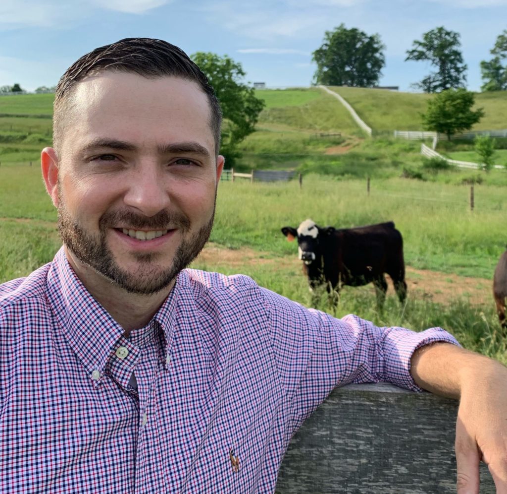 portrait image of a man with a field and cow in the background