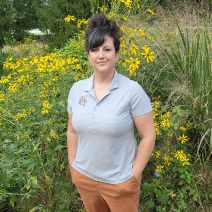 Celia in QF shirt_Sept 2021 woman standing next to native plants